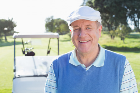 Happy golfer smiling at camera with golf buggy behind on a sunny day at the golf courseの写真素材