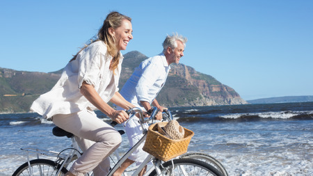 Smiling couple riding their bikes on the beach on a sunny dayの写真素材