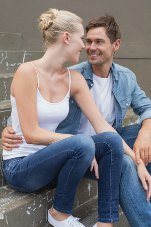 Hip young couple sitting on steps smiling at each other on a sunny day in the cityの写真素材