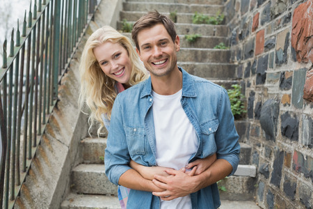 Hip young couple sitting on steps smiling at camera on a sunny day in the cityの写真素材