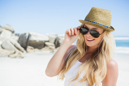 Stylish blonde smiling at camera on the beach on a sunny dayの写真素材