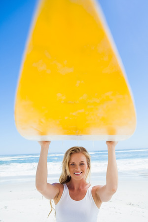 Blonde surfer holding her board smiling at camera on a sunny dayの写真素材