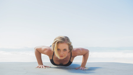 Fit blonde in plank position on the beach on a sunny day