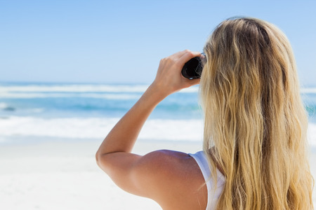 Blonde looking to the ocean through binoculars on a sunny dayの写真素材