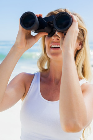 Blonde looking through binoculars on the beach on a sunny dayの写真素材