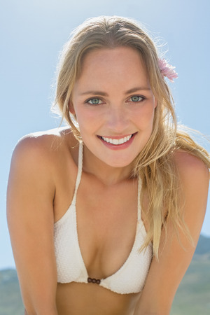 Beautiful blonde in white bikini smiling at camera on the beach on a sunny dayの写真素材