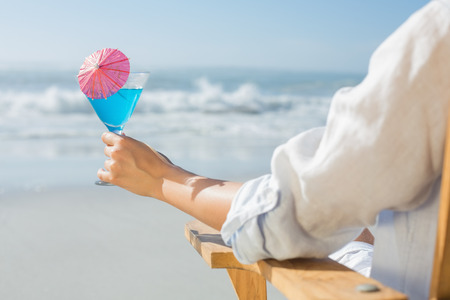 Woman relaxing in deck chair by the sea holding cocktail on a sunny dayの写真素材
