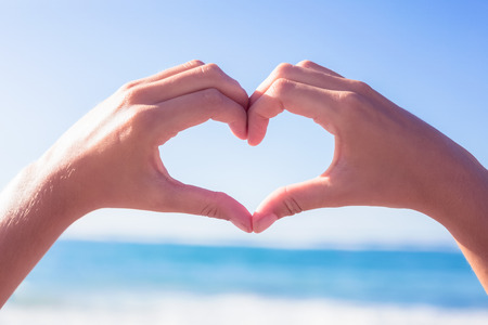 Hands making heart shape on the beach on a sunny day