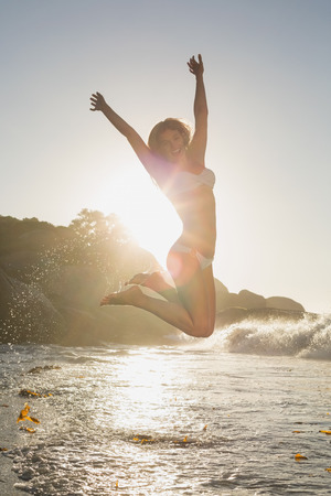 Beautiful jumping blonde in white bikini at the beach on a sunny dayの写真素材