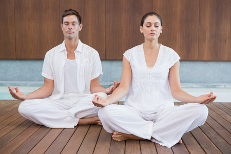 Attractive couple in white meditating in lotus pose in health spaの写真素材