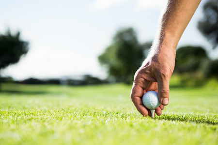 Golfer placing golf ball on tee on a sunny day at the golf courseの写真素材