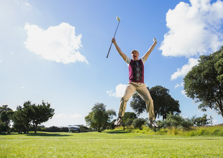 Excited golfer jumping up holding club on a sunny day at the golf courseの写真素材