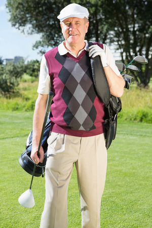 Golfer carrying his golf bag smiling at camera on a sunny day at the golf courseの写真素材
