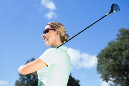 Female golfer standing holding her club smiling on a sunny day at the golf courseの写真素材