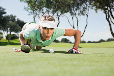 Female golfer blowing her ball on putting green on a sunny day at the golf courseの写真素材