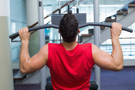 Strong bodybuilder using weight machine for arms at the gym