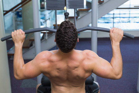 Shirtless bodybuilder using weight machine for arms at the gym