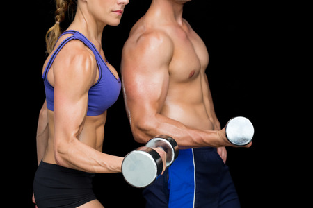 Bodybuilding couple posing with large dumbells on black backgroundの写真素材