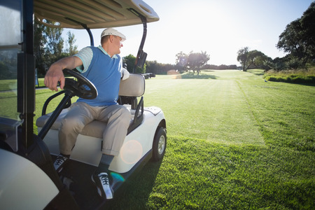 Golfer driving his golf buggy in reverse on a sunny day at the golf courseの写真素材