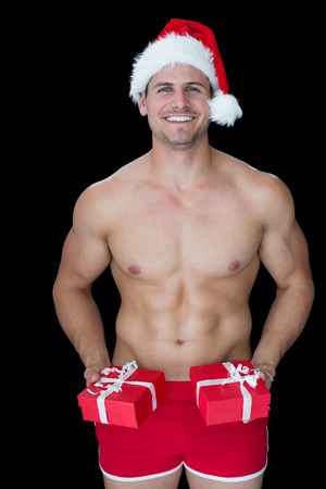 Smiling muscular man posing in sexy santa outfit offering gifts on black backgroundの写真素材