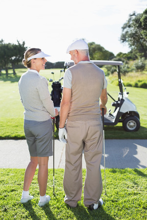 Happy golfing couple smiling at each other on a sunny day at the golf courseの写真素材