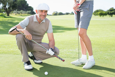 Golfing couple on the putting green with man smiling at camera on a sunny day at the golf courseの写真素材
