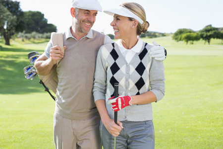 Golfing couple smiling at each other on the putting green on a sunny day at the golf courseの写真素材