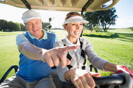 Happy golfing couple sitting in golf buggy on a sunny day at the golf courseの写真素材