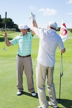 Golfing friends high fiving on the eighteenth hole on a sunny day at the golf courseの写真素材