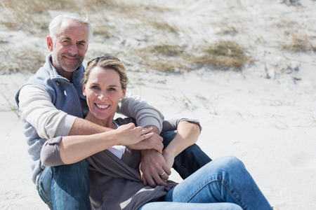 Attractive couple smiling at camera on the beach on a bright but cool dayの写真素材