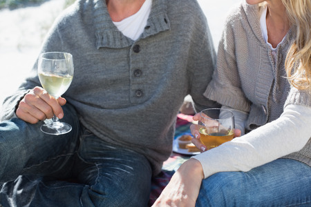 Couple enjoying white wine on picnic at the beach on a bright but cool day