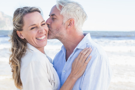 Man kissing his smiling partner on the cheek at the beach on a sunny dayの写真素材