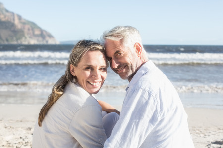 Couple sitting on the beach under blanket smiling at camera on a sunny dayの写真素材