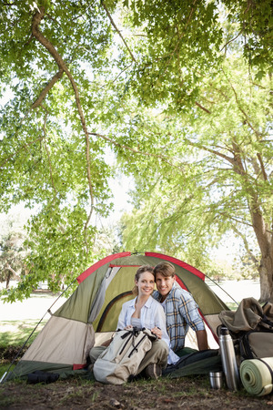 Happy couple sitting in their tent after a hike and looking at camera on a sunny dayの写真素材