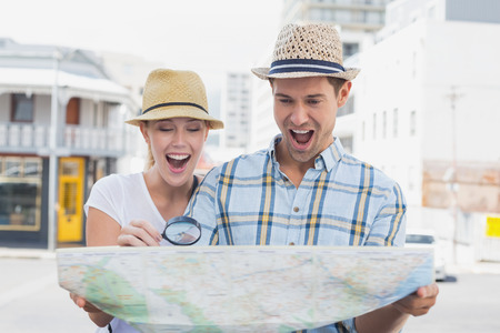 Young tourist couple consulting the map with magnifying glass on a sunny day in the city