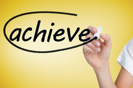 Businesswoman writing the word achieve against yellow vignetteの写真素材