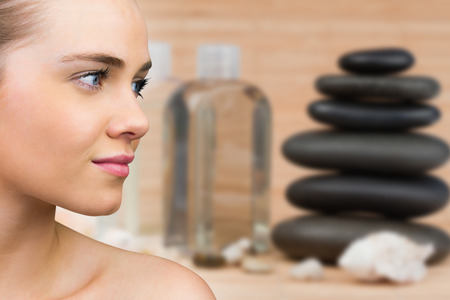 Smiling blonde natural beauty against stack of pebbles with beauty productsの写真素材