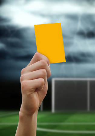 Hand holding up yellow card against football pitch under stormy skyの写真素材