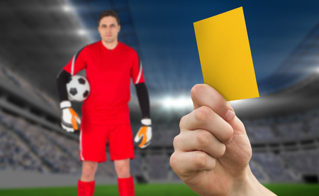 Hand holding up yellow card against football stadium with goalieの写真素材