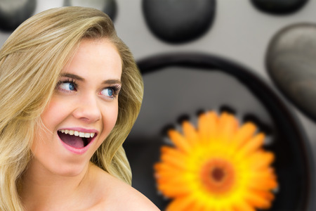 Smiling blonde natural beauty against orange flower floating in bowl with pebblesの写真素材