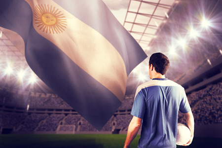 Handsome football player holding the ball against football stadiumの写真素材