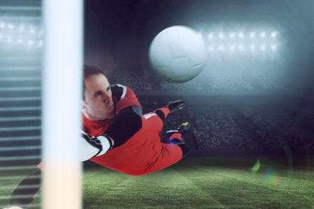 Fit goal keeper jumping up against large football stadium under blue skyの写真素材