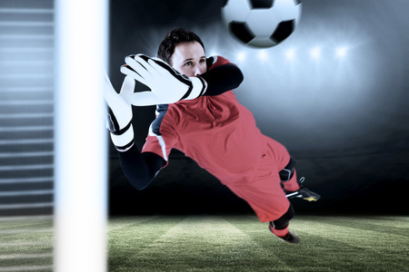 Fit goal keeper jumping up against football pitch under spotlightsの写真素材