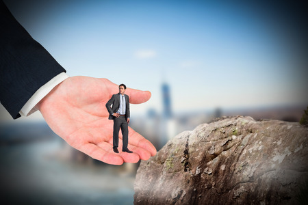 Serious businessman with hand on hip in large hand against large rock overlooking foggy cityの写真素材