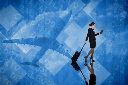 Businesswoman pulling her suitcase holding tablet against airport departures board for south americaの写真素材