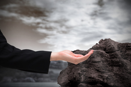 Businesswomans hand presenting against large rock overlooking foggy forestの写真素材