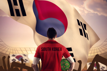 South korea football player holding ball against large football stadium under bright blue skyの写真素材