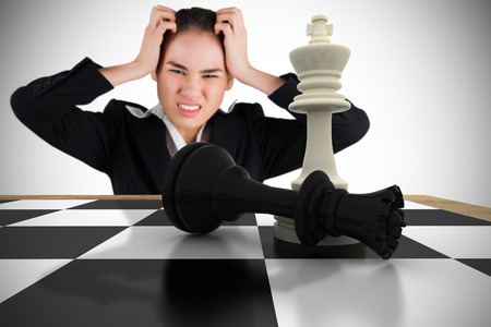 Stressed businesswoman with hands on her head with chessboard against white background with vignetteの写真素材