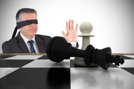 Mature businessman in a blindfold with chessboard against white background with vignetteの写真素材