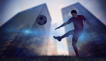 Football player in red kicking against low angle view of skyscrapersの写真素材